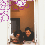 Twee vrouwen hangen uit een raam en kijken naar beneden naar iets buiten beeld. De tekst leest: Hoe nieuwsgierig kan JIJ zijn?